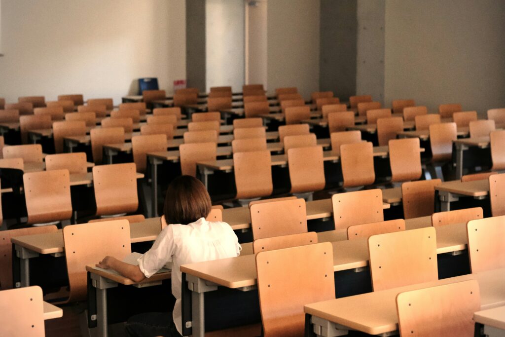 Prüfungsangst im Studium – Allein mit dem Druck Eine einzelne Person sitzt in einem ansonsten leeren Hörsaal – Symbolbild für Prüfungsangst, Überforderung und Einsamkeit im Studium.