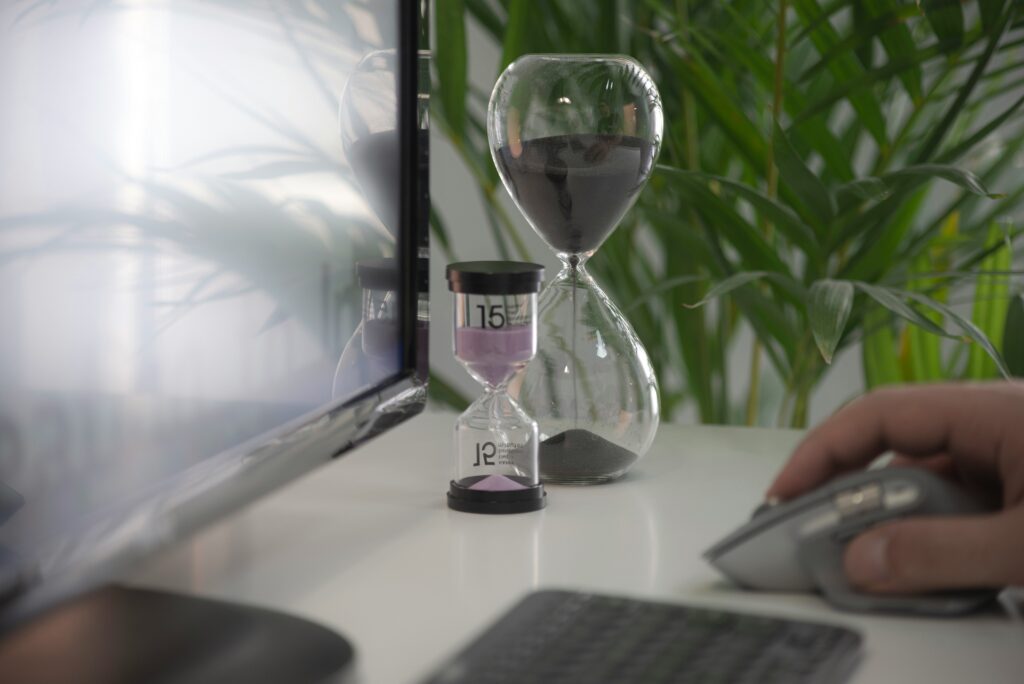 Zeitmanagement Ein Schreibtisch mit Sanduhren, einem Bildschirm und einer Tastatur sind zu sehen.
