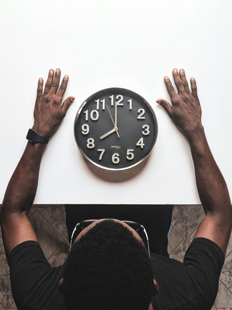 Person sitzt an einem Tisch und blickt auf eine Wanduhr – Symbolbild für Prokrastination und Zeitdruck im Studium
