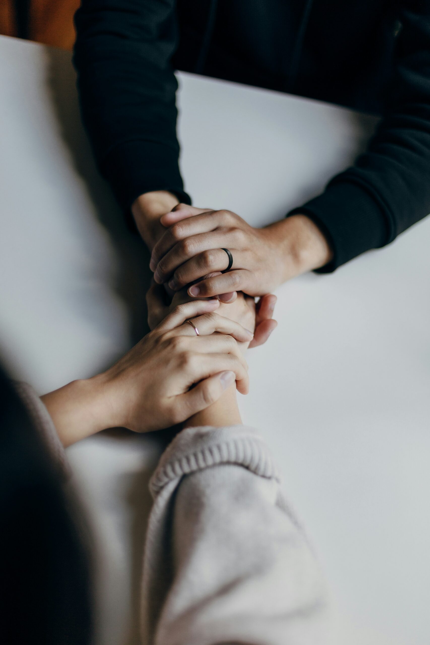 Psychologische Hilfe - Symbolbild Zwei Personen halten sich an einem Tisch einfühlsam die Hände – Symbol für Unterstützung und Mitgefühl.