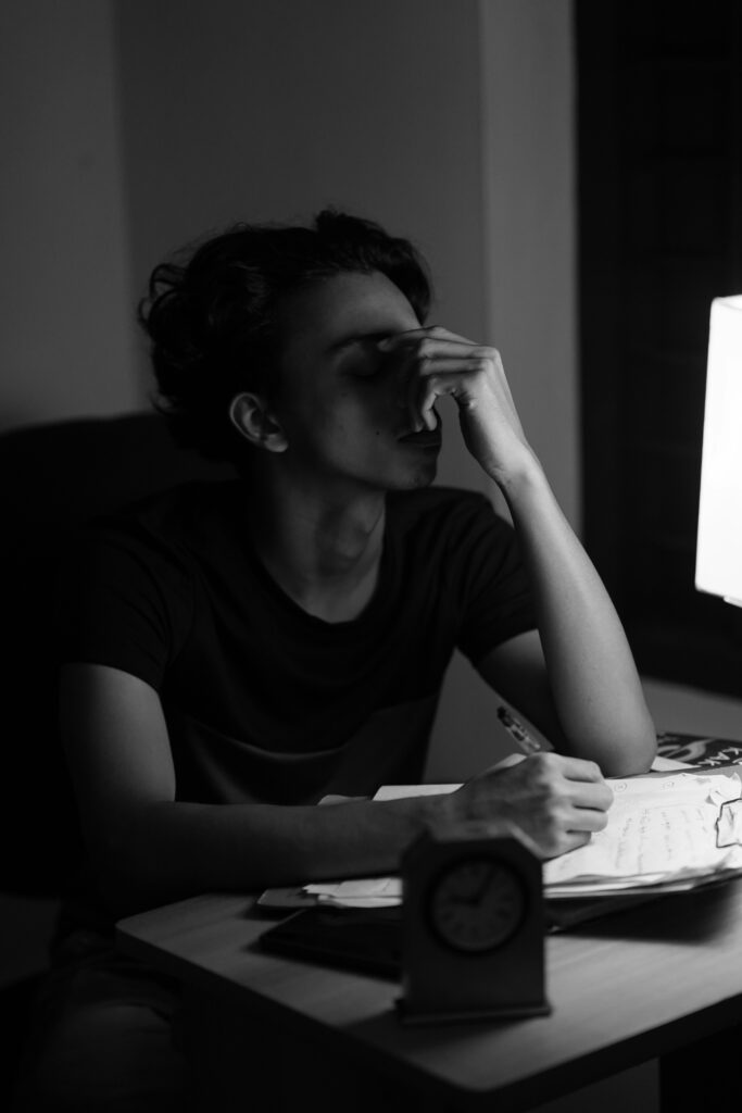Student sitzt erschöpft am Schreibtisch, stützt den Kopf in die Hand, umgeben von Lernmaterial – Ausdruck mentaler Belastung im Studienalltag.