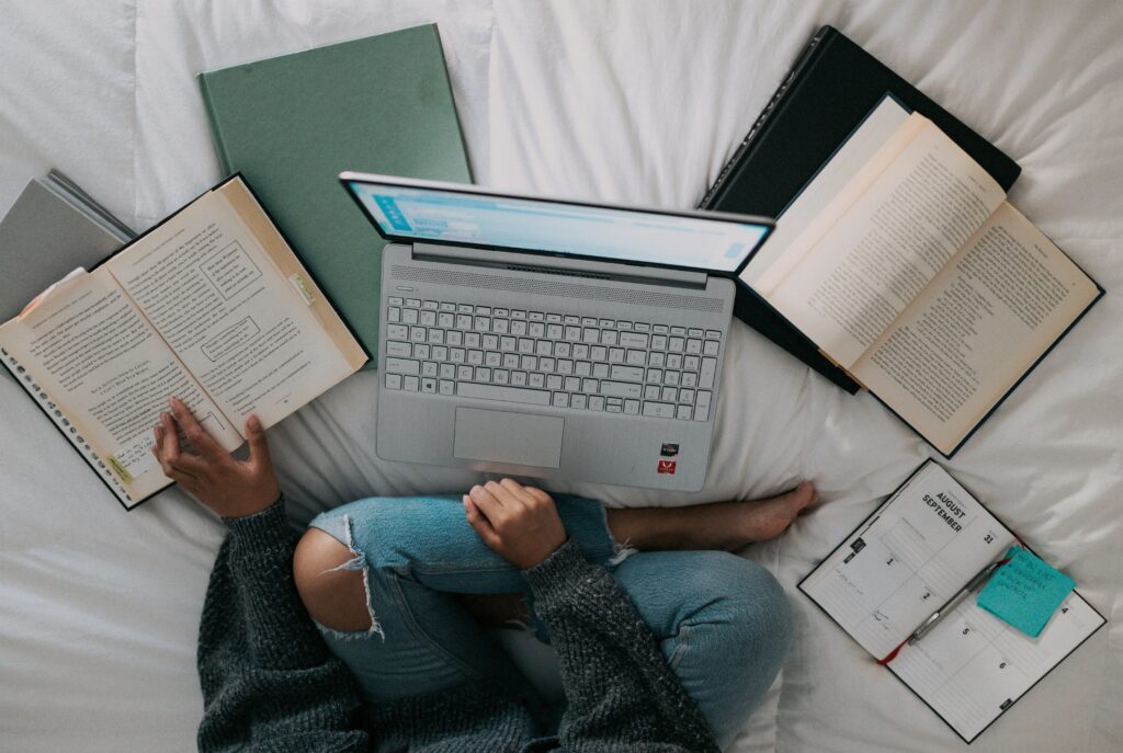 Frau in blauem Hemd sitzt mit Laptop entspannt auf dem Bett.