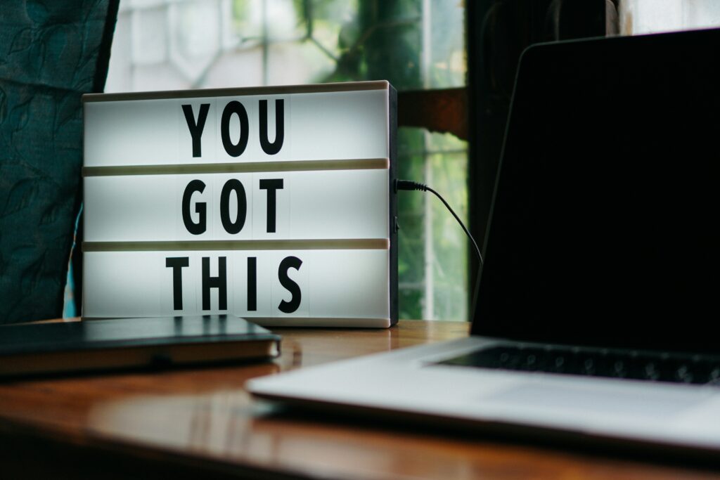 Eine beleuchtete Leuchttafel mit der Aufschrift "YOU GOT THIS" steht auf einem Schreibtisch neben einem Laptop.